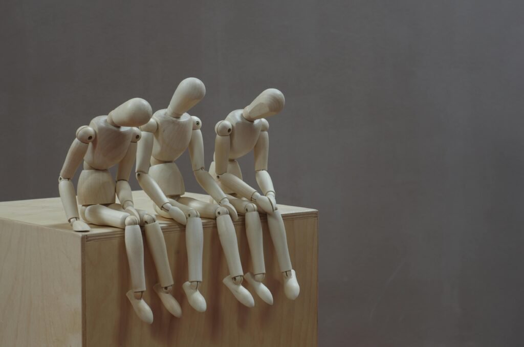Three wooden mannequins in thoughtful poses on a wooden block against a neutral background.